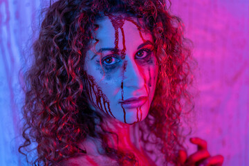 close-up of a girl with curly hair and a bloodied face with ruined make-up with purple and blue...