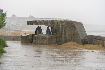 Asnelles-Sur-Mer, France - 08 03 2021:  Three people waiting under a blockhouse for the rain to end - obrazy, fototapety, plakaty