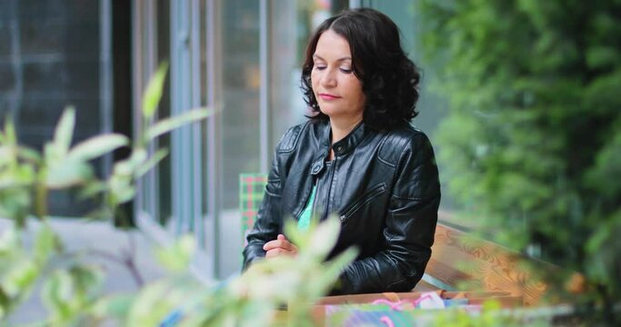 A girl is sitting at a table on the street. Her phone rang and she started a conversation. The girl is talking emotionally on her smartphone. A beautiful brunette is talking on the phone.