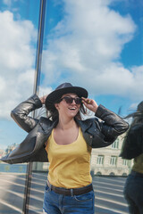 Beautiful woman with hat and sunglasses near the mirror wall of city building