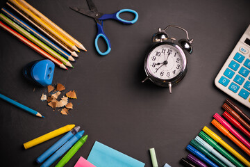 Colorful stationery, alarm clock and supplies on chalkboard background