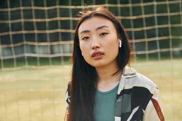 Against net of sport field. Young asian woman is outdoors at daytime