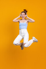 Fototapeta na wymiar Vertical image of young cute girl jumping isolated on yellow studio background. Female fashion model in casual clothes. Concept of human emotions, natural beauty, youth
