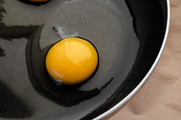Top view on a raw egg with bright yellow yolk and transparent white with a clots in a black frying...