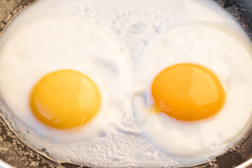 Two bright round raw yolks in whites in a frying pan. Cooked tender, soft fried eggs is a simple breakfast in light of sun. Top view, close-up