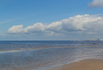 Beautiful sandy shore of the calm northern baltic sea with green stones, blue sky with big white clouds in sunny weather