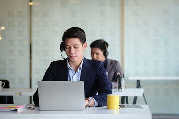 Asian man operator wearing wireless headset working in customer care support service team office.