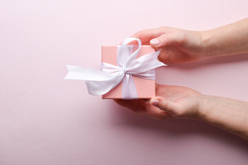 A woman's hand holds a pink gift box with a white bow on a pink background