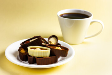 A plate with chocolates and a cup of coffee on a yellow background.