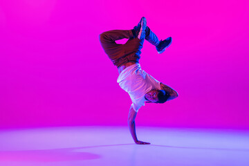 Young stylish man, hip-hop dancer dancing solo in modern clothes isolated over bright magenta background at dance hall in neon light.