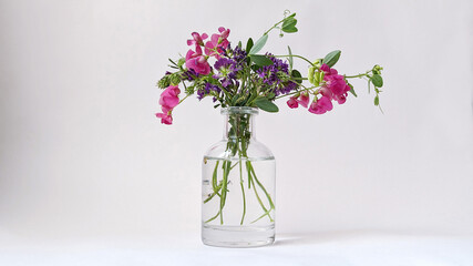 A bouquet of pink and lilac wildflowers in a small transparent vase on a white background © Аля Джамамедова
