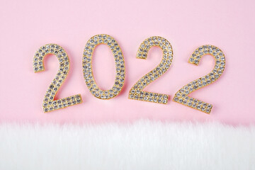 Gold numbers with diamonds, precious stones on a pink background with white fur.A greeting card for Christmas 2022, a banner, an invitation to a party for jewelry stores,beauty salons, for women.