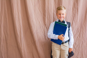 Cheerful smiling schoolboy boy returning to school holding a book on studio background. Empty space