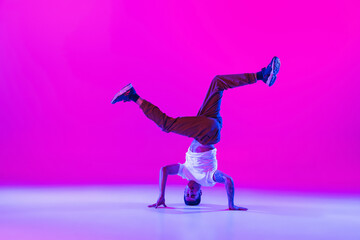 Fototapeta na wymiar Young stylish man, break dancing dancer practicing solo in modern clothes isolated over bright magenta background at dance hall in neon light.