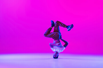 Fototapeta na wymiar Portrait of young man, break-dance dancer dancing solo in modern clothes isolated over bright magenta background at dance hall in neon light.
