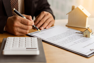 A home agent sitting at a desk in the office with a house plan with contract documents and a home buying idea, insurance or real estate loan idea calculator.