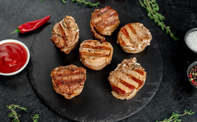 cooked grilled pork tenderloin medallions wrapped in bacon on stone background