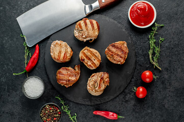 cooked grilled pork tenderloin medallions wrapped in bacon on stone background