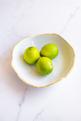 3 limes in a fruit bowl on marble surface