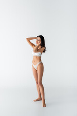 full length of young barefoot and cheerful woman in lingerie posing on white