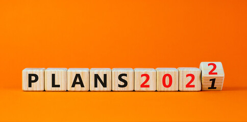 2022 plans new year symbol. Turned a wooden cube and changed words 'Plans 2021' to 'Plans 2022'. Beautiful orange background, copy space. Business, 2022 plans new year concept.