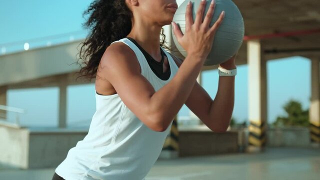 A Focused African American Woman Doing Squats Outside While Holding A Ball In The Morning