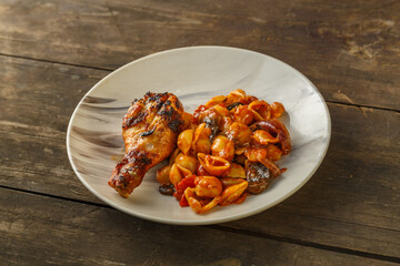 Seashell pasta in tomato with chicken leg baked on the grill on a wooden table.