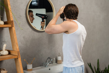 man in white tank top drying hair near mirror in bathroom - obrazy, fototapety, plakaty