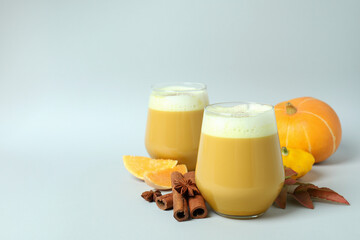 Glasses of pumpkin latte and ingredients on light gray background