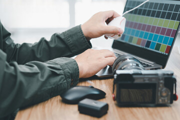 Close up hand photographer typing on laptop keyboard for adjust program in Display Calibration and camera battery on the wood table