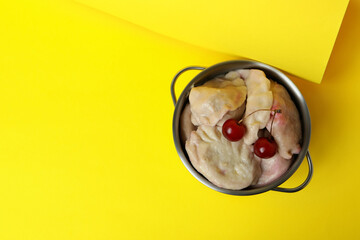 Pot with pierogi with cherry on yellow background