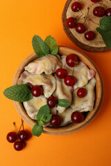 Wooden bowl with pierogi with cherry on orange background