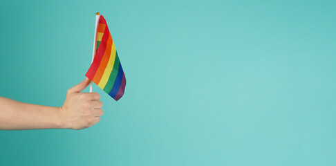 Fototapeta premium LGBT concept.Hand is holding a rainbow flag on mint green or tiffany blue background.