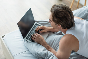 Naklejka premium high angle view of brunette man typing on laptop with blank screen in bed