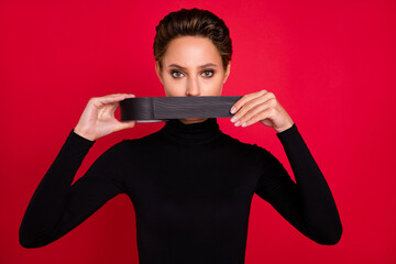 Photo of young serious woman hold hands adhesive tape speech cover mouth freedom isolated on red color background