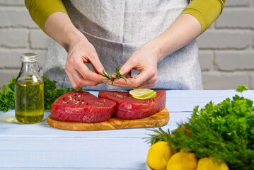 Raw tuna fillet steak with dill, lemon and spices in olive cutting board, ready for cooking