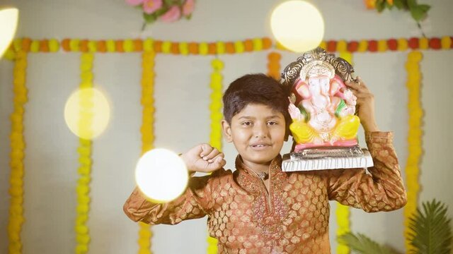 Happy smiling kid with ganesha idol on shoulder saying or chanting ganapati bappa morya during festival celebrations.