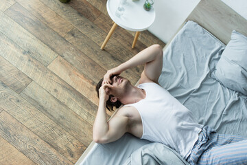 high angle view of man covering eyes with hands while suffering from hangover in bed