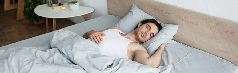 Obraz na płótnie Canvas young brunette man sleeping on blue bedding in morning, banner