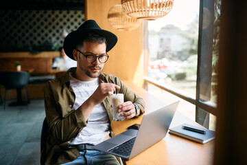 Young student uses laptop and e-learns while drinking coffee in cafe.