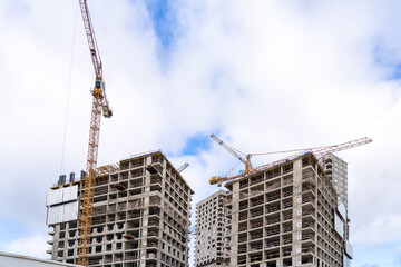 Construction cranes and unfinished residential buildings against blue sky with clouds. Housing construction, apartment block with scaffolding