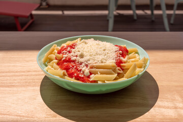 Plate of Italian macaroni with bolognese sauce and grated parmesan cheese on a light wooden table