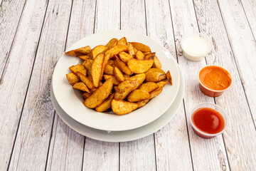 Large portion of French fries cut into wedges with assorted sauces to dip