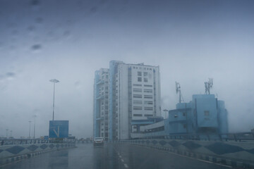 Obraz premium Raindrops falling on car windshield glass, abstract blurs of Nabanna building , state administrative office. Monsoon stock image of Howrah city , West Bengal, India