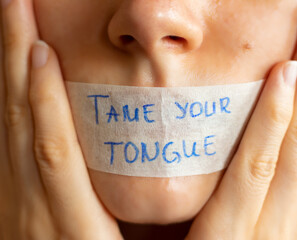 Tame (control) your tongue handwritten Bible quote on plaster on woman's lips. Christian teaching power of mouth words.  A closeup. - obrazy, fototapety, plakaty