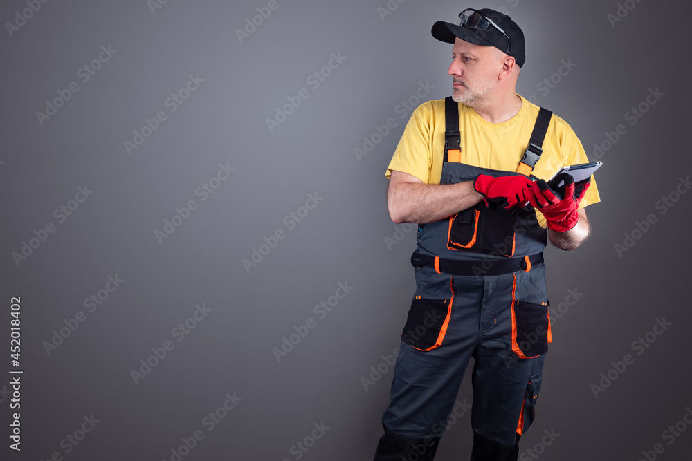 Poster a man in work gloves holds a smartphone and looks away. a worker with a tablet computer on a gray ba