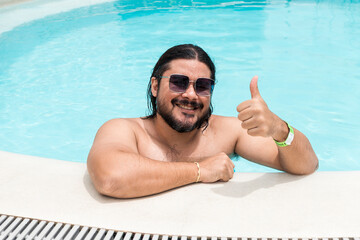 A bearded tourist of mixed race gives his seal of approval. A thumbs up gesture. Positive review of the resort and swimming pool. - Powered by Adobe