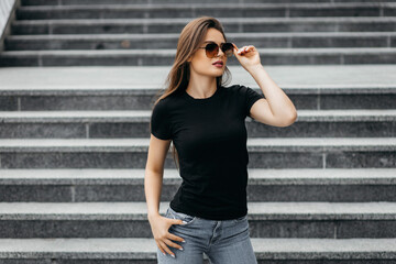 Stylish brunette girl wearing black t-shirt and glasses posing against street , urban clothing...