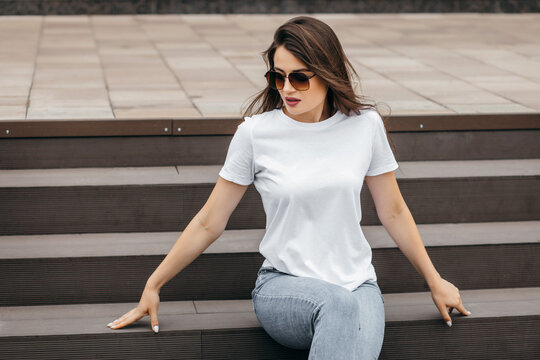 Stylish brunette girl wearing white t-shirt and glasses posing against street , urban clothing style. Street photography