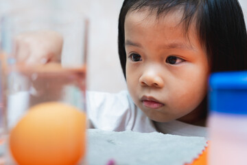 Cute girl doing a simple science experiment, the floating egg experiment. Asian child is observing...